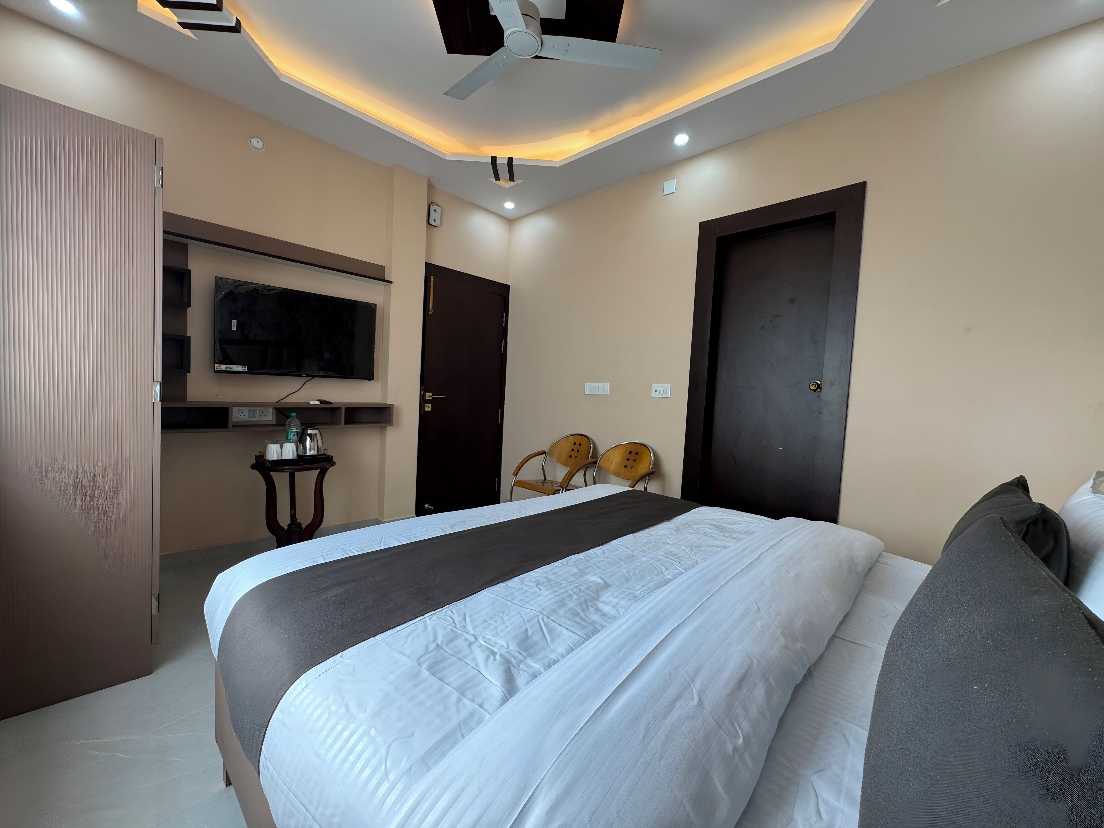 Habitación de hotel moderna con una cama grande, un televisor de pantalla plana montado en la pared, una mesita con una botella de agua y dos sillas.