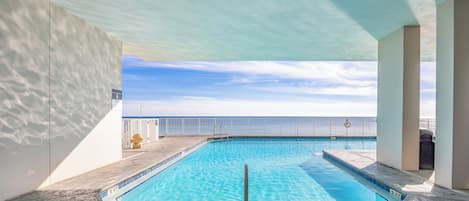 Una piscina con agua azul cristalina, rodeada por un muro blanco y una barandilla, con vistas al océano en el fondo.