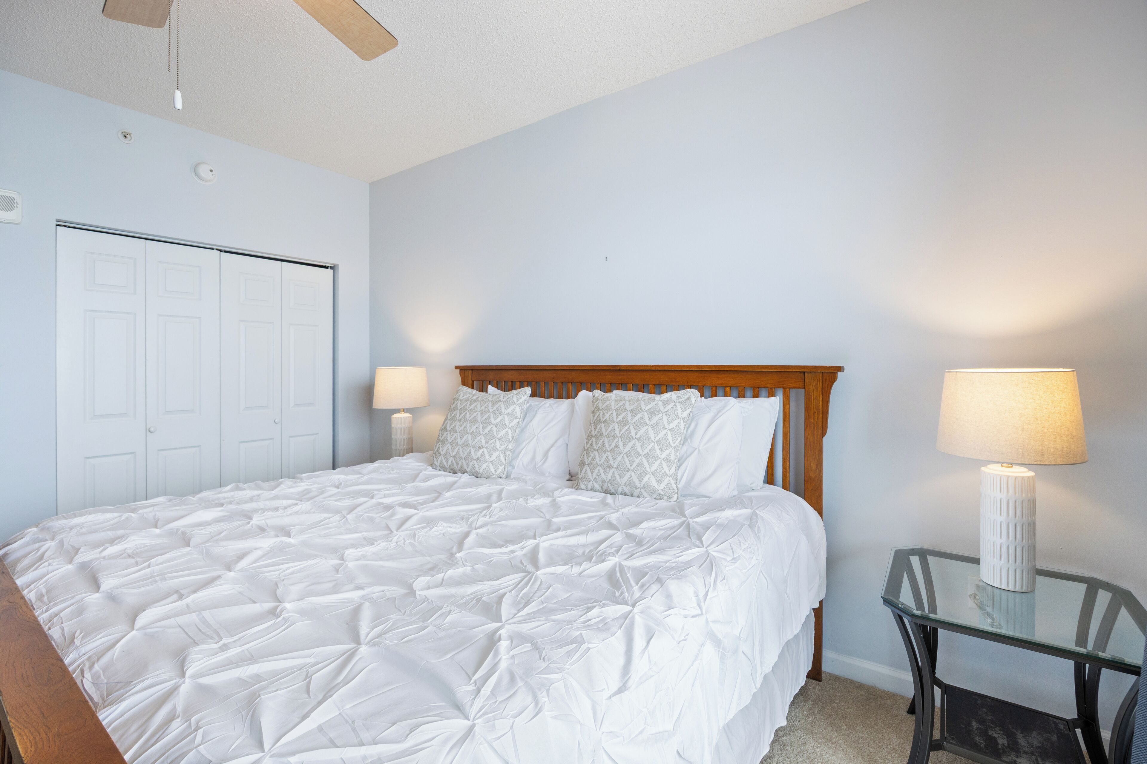 A bedroom with a bed, a wooden headboard, two bedside lamps, and a glass table.