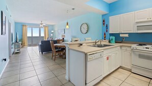 A modern kitchen with white cabinets, a built-in dishwasher, and a double oven. There is a dining area with a table and chairs, and a large window with curtains. - New Listing! Forever View From The 7th Floor At Popular Windemere Resort! (Pensacola)