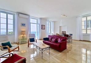A spacious living room with a red sofa, wooden chairs, a coffee table, and large windows.