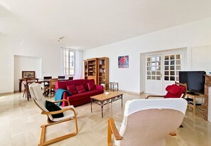 Ein geräumiges Wohnzimmer mit einem roten Sofa, einem Holztisch, einem roten Sessel, einem Fernseher und einem Bücherregal.