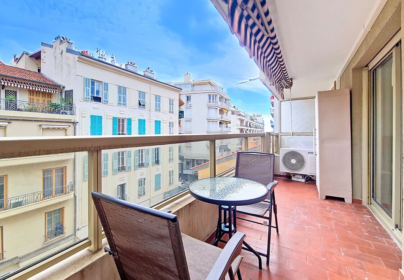 A balcony with a table and chairs, a fan, and a view of neighboring buildings.