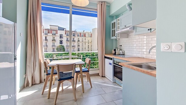 Eine moderne Küche mit Essbereich, Blick auf Gebäude und einem Balkon mit Vorhängen.