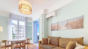 Ein modernes Wohnzimmer mit einem stehenden Sofa, einem Esstisch mit Stühlen und einem großen Fenster mit Blick auf Gebäude.