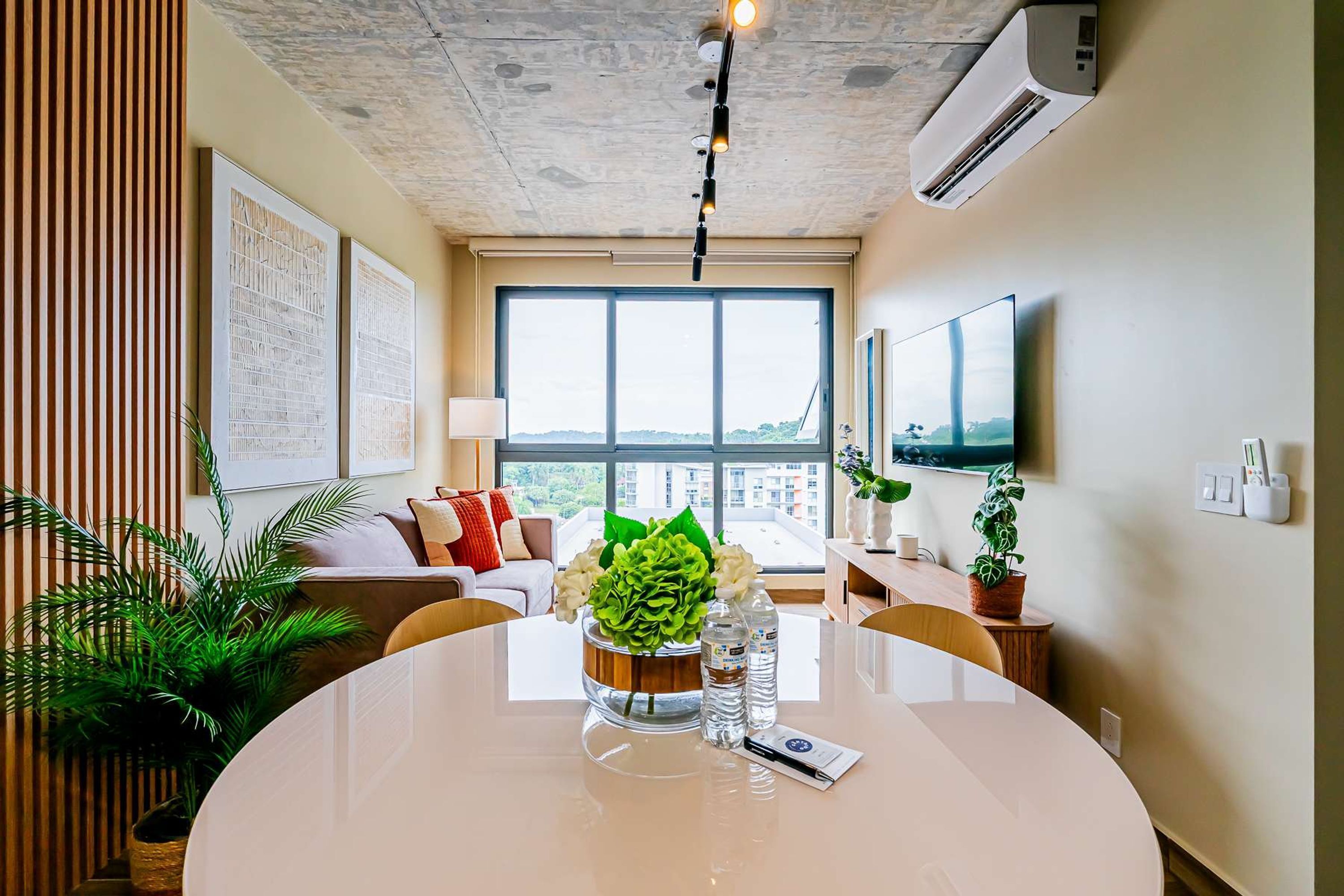 A modern living room with a large window, a flat-screen TV, and a dining area with a table set for two.