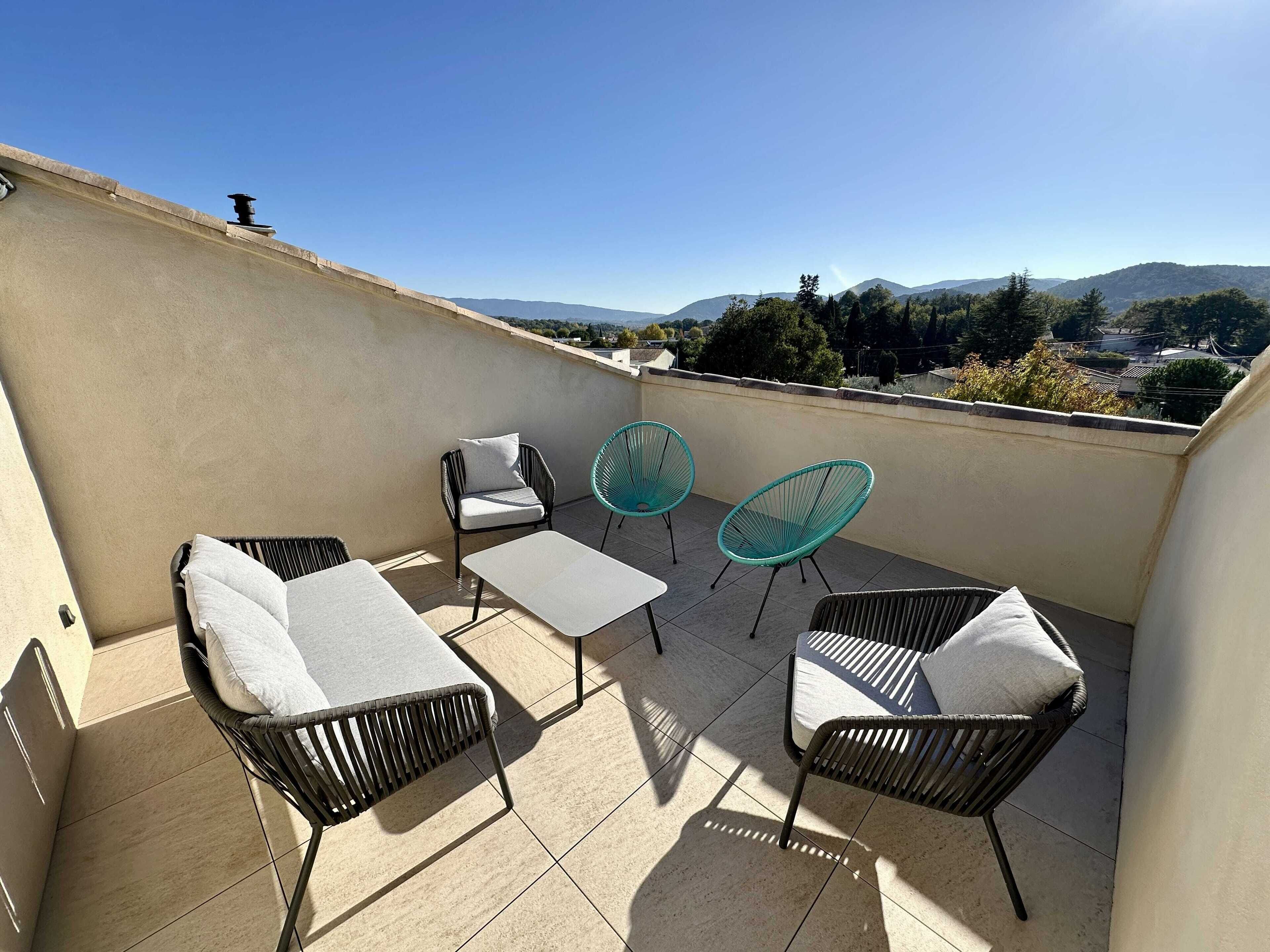 A rooftop terrace with four chairs, two tables, and a view of distant hills.