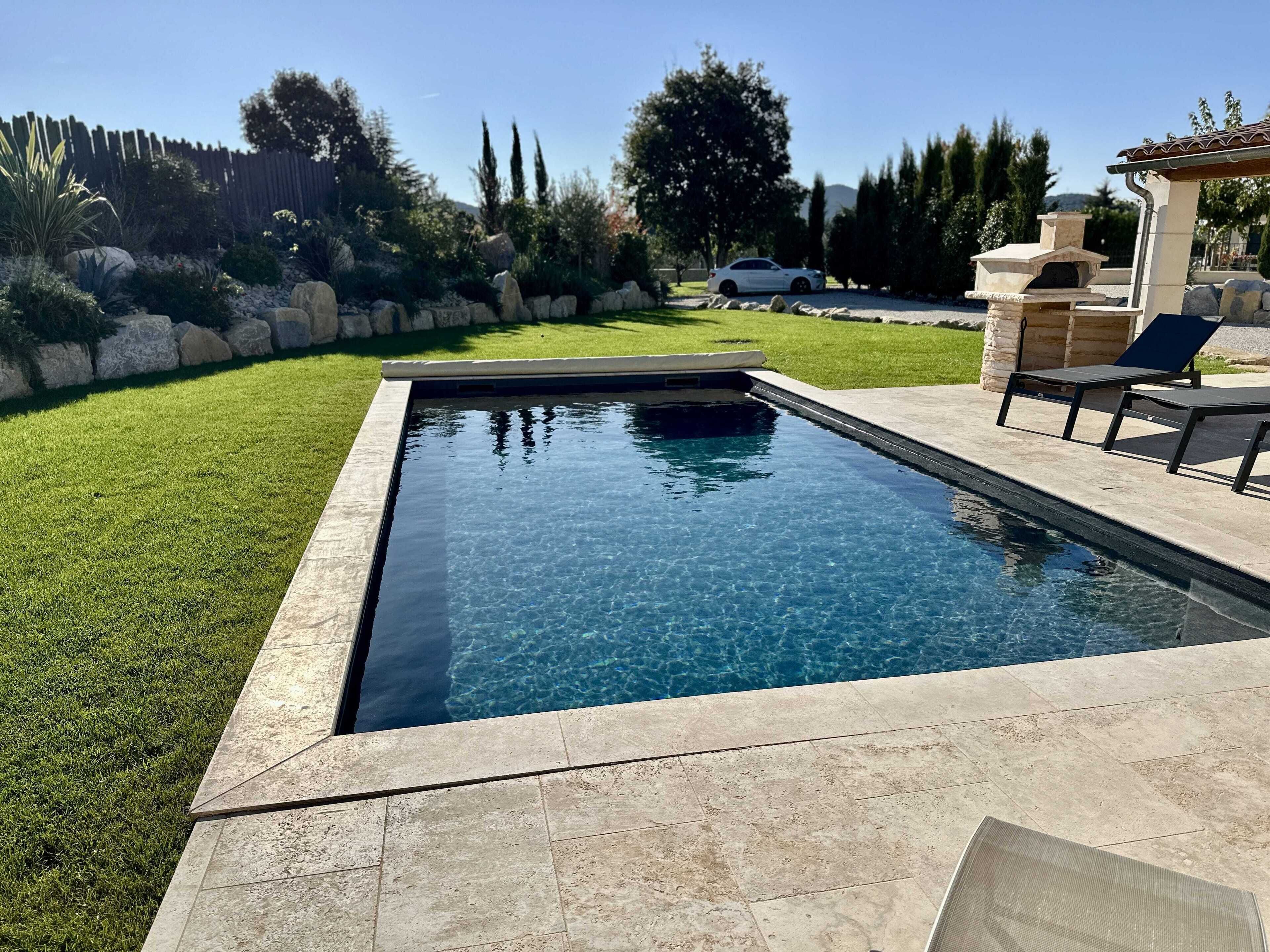 Una piscina rectangular con borde de piedra, rodeada por un césped cuidado y un muro de piedra.
