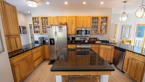 A modern kitchen with wooden cabinets, a black countertop, stainless steel appliances, and a central island with stools. - Oversized Family Resort Home w/Golf Cart (Michigan City)