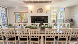 A dining area with a large round table, white chairs, a fireplace, and a view of the outdoors. - Oversized Family Resort Home w/Golf Cart (Michigan City)