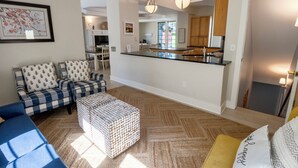 A modern living room with a sofa, ottoman, and a dining area with chairs. - Oversized Family Resort Home w/Golf Cart (Michigan City)