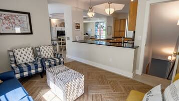 Un salon moderne avec un canapé, un pouf et un coin repas avec des chaises.