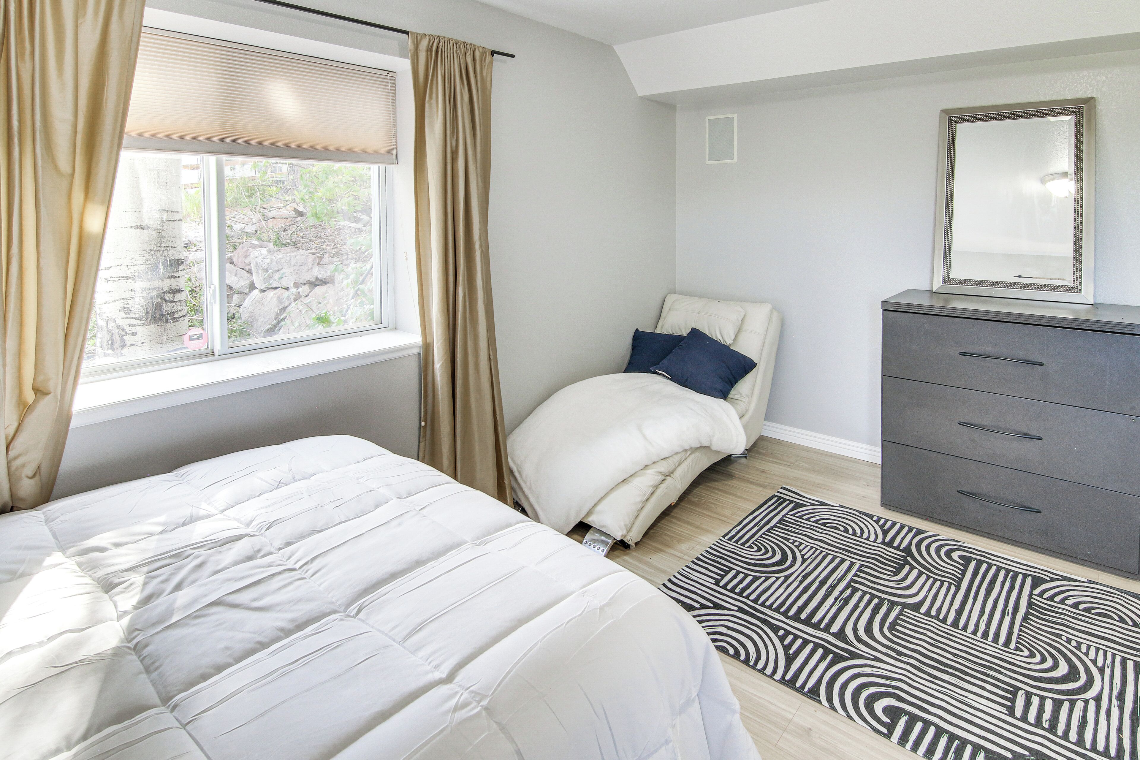 A bedroom with a bed, a dresser, a mirror, and a window with curtains.