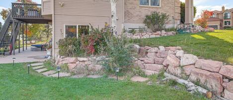 A two-story house with a stone retaining wall, a covered outdoor staircase, and a well-maintained lawn.
