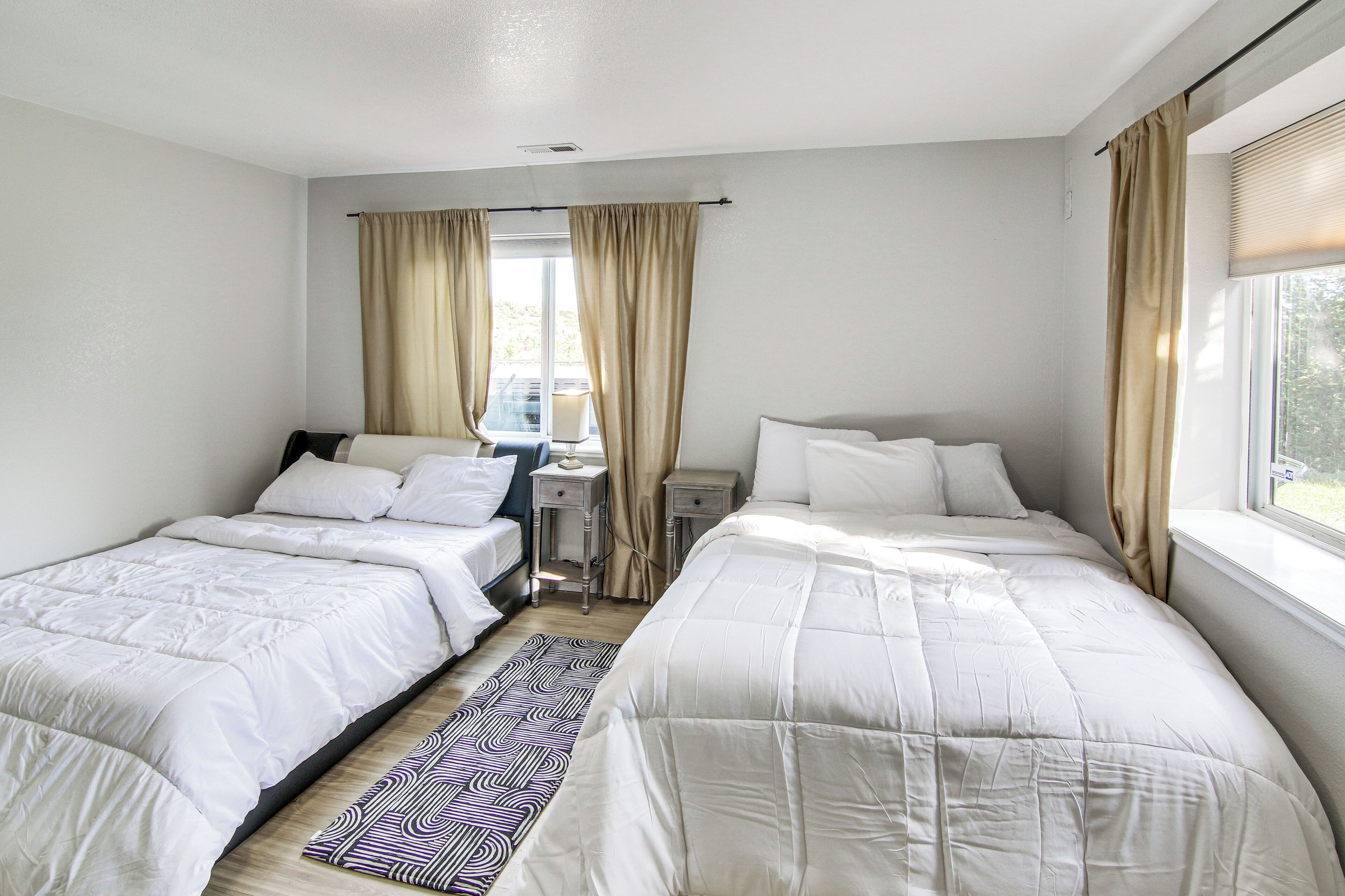 A hotel room with two beds, a desk, and a window with curtains.