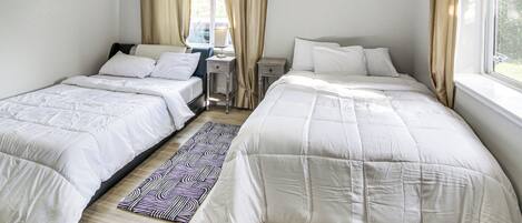 A hotel room with two beds, a desk, and a window with curtains.