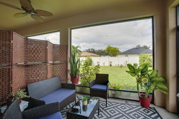 Eine überdachte Terrasse mit Korbmöbeln, Blumentöpfen und Blick auf einen Garten.