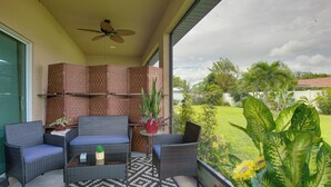 Ein Balkon mit Korbmöbeln, einem Deckenventilator und Blick auf eine grüne Landschaft.