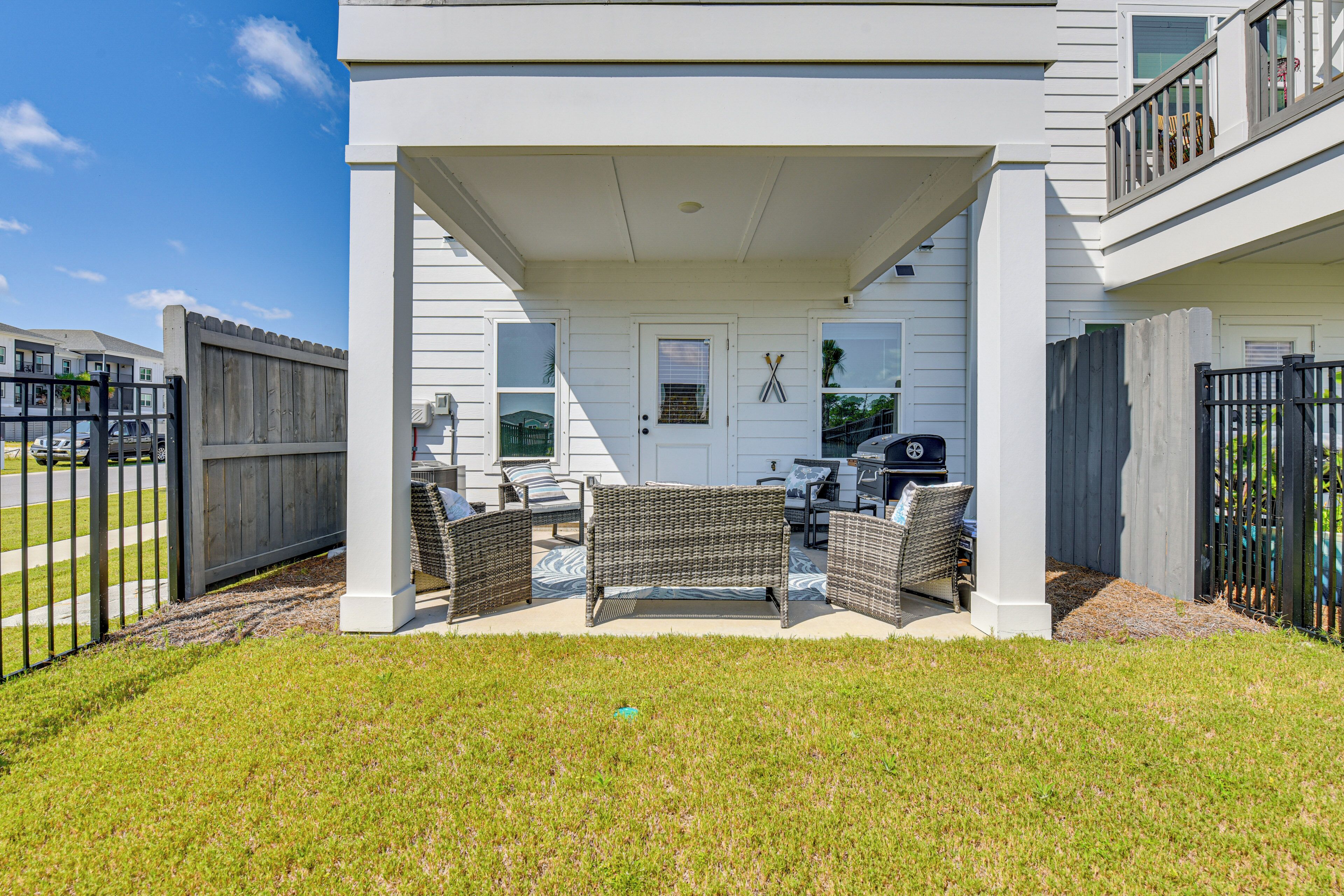 A covered outdoor seating area with wicker furniture, a grill, and a white door with a window.