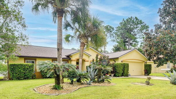 A yellow house with a well-maintained lawn, palm trees, and various shrubs. - 5 Mi to Beaches: Family Getaway in Palm Coast! (Palm Coast)