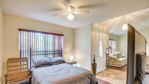 A bedroom with a bed, a chair, a ceiling fan, a television, and a door leading to another room. - 5 Mi to Beaches: Family Getaway in Palm Coast! (Palm Coast)