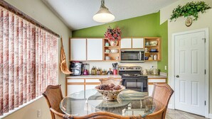 A dining area with a glass table and wicker chairs, a kitchen with wooden cabinets and appliances, and a green accent wall. - 5 Mi to Beaches: Family Getaway in Palm Coast! (Palm Coast)