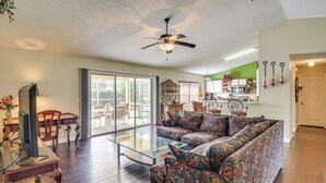 A spacious living room with a glass coffee table, a sofa, and a ceiling fan. - 5 Mi to Beaches: Family Getaway in Palm Coast! (Palm Coast)