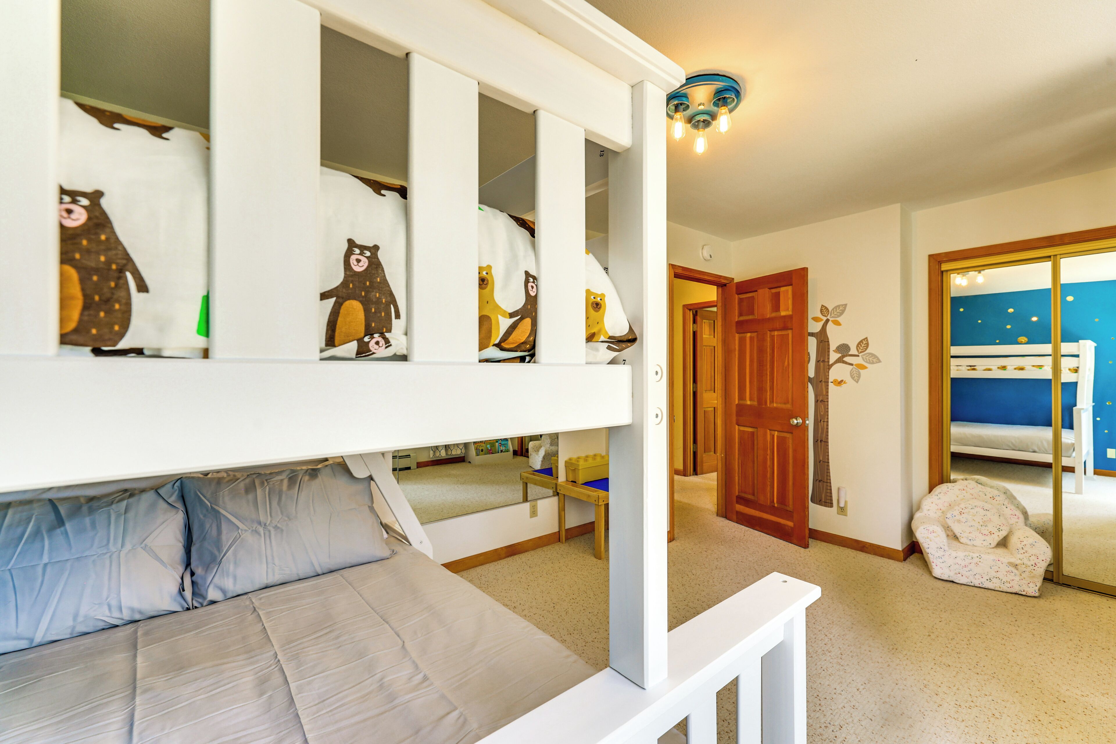 Un lit superposé pour enfant avec une literie à motifs d’ours, une porte en bois et un mur bleu orné d’un motif en forme d’étoile.