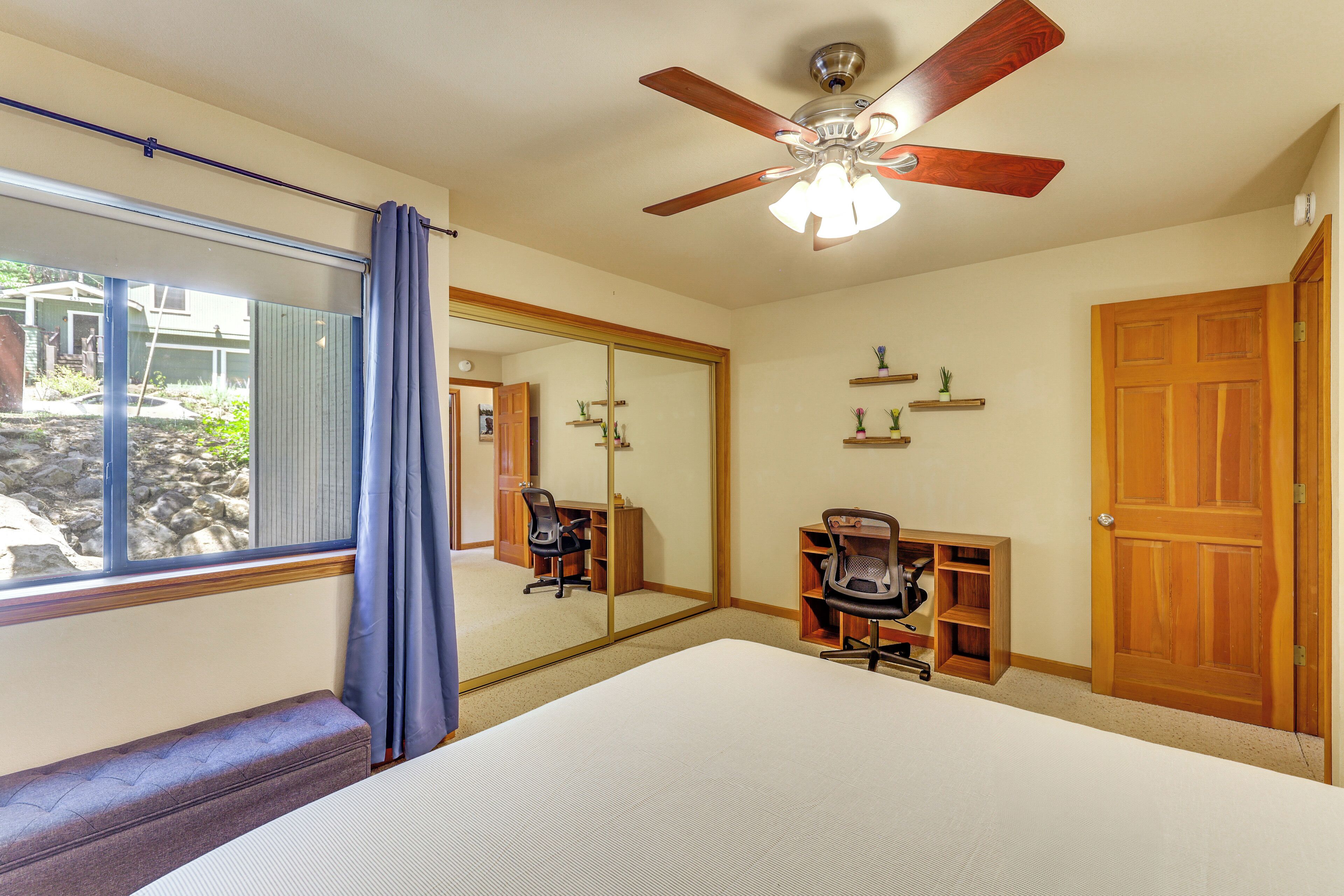 A bedroom with a large bed, a ceiling fan, a desk with a chair, a mirror, and a wardrobe.