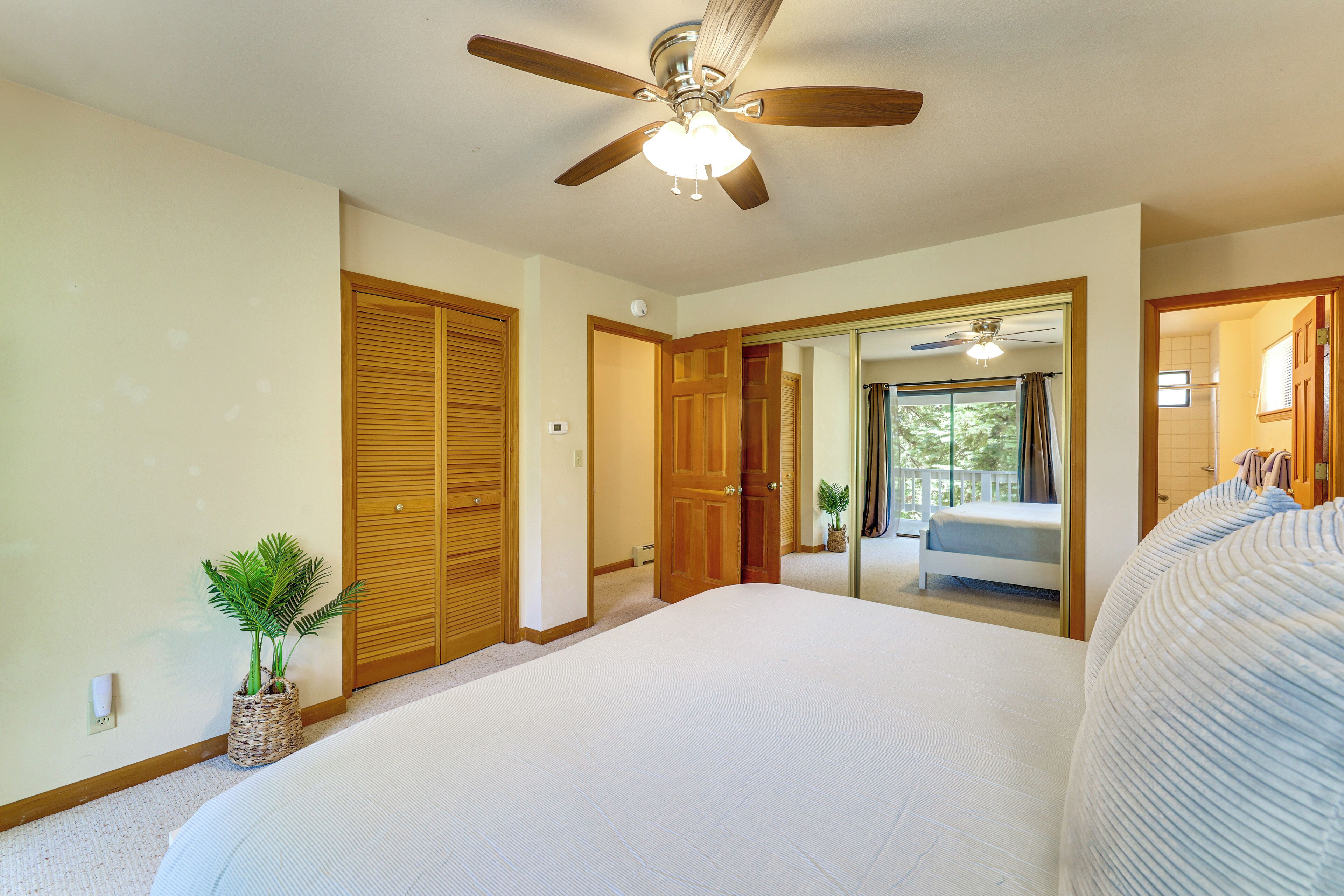 A bedroom with a large bed, a ceiling fan, wooden closets, and a view of a balcony.