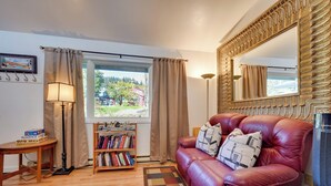 A cozy living room with a leather sofa, a bookshelf, a lamp, and a large mirror. - 2 Mi to Bishops Beach: Mtn-view Escape w/ Deck (Homer)