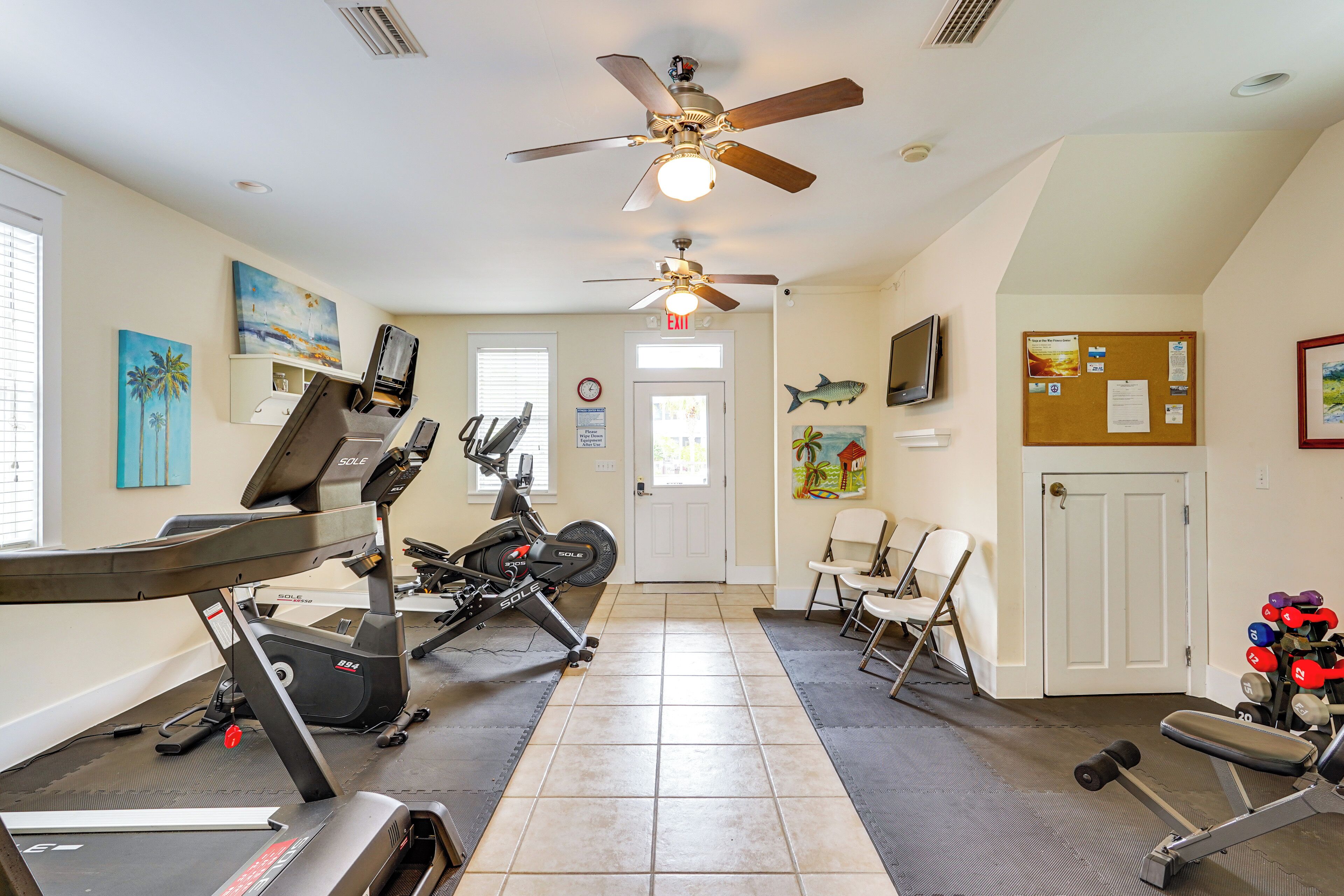 A home gym with exercise equipment, a ceiling fan, and artwork on the walls.