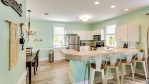 A kitchen with a central island, white cabinets, a stainless steel refrigerator, and a dining area with wooden chairs. - Steps to Sea! Cottage w/ Pools in Port St Joe (Port St. Joe)