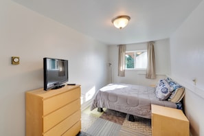 A bedroom with a bed, a TV on a wooden dresser, a window with curtains, and a ceiling light. - Fish & Hike! Home Base for Kachemak Bay Adventures (Homer)