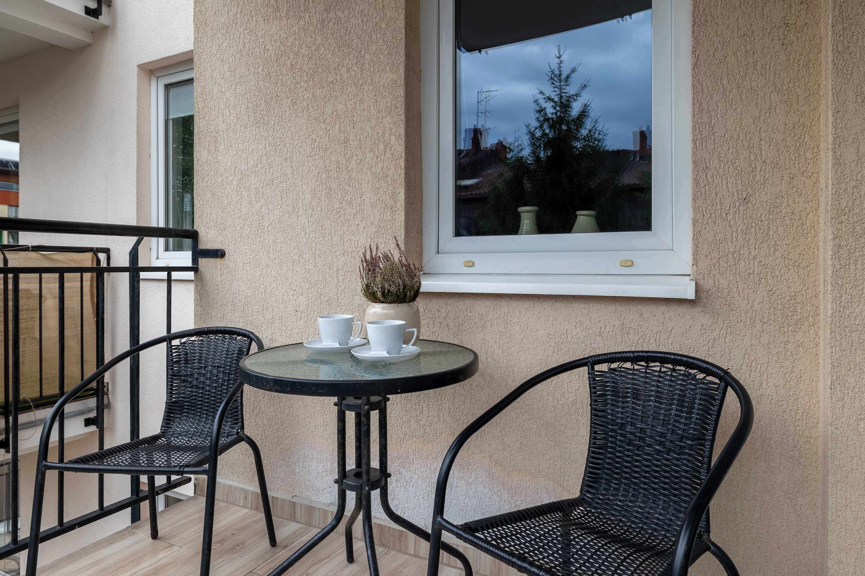 Un balcon avec deux fauteuils en osier, une petite table ronde et une plante en pot.