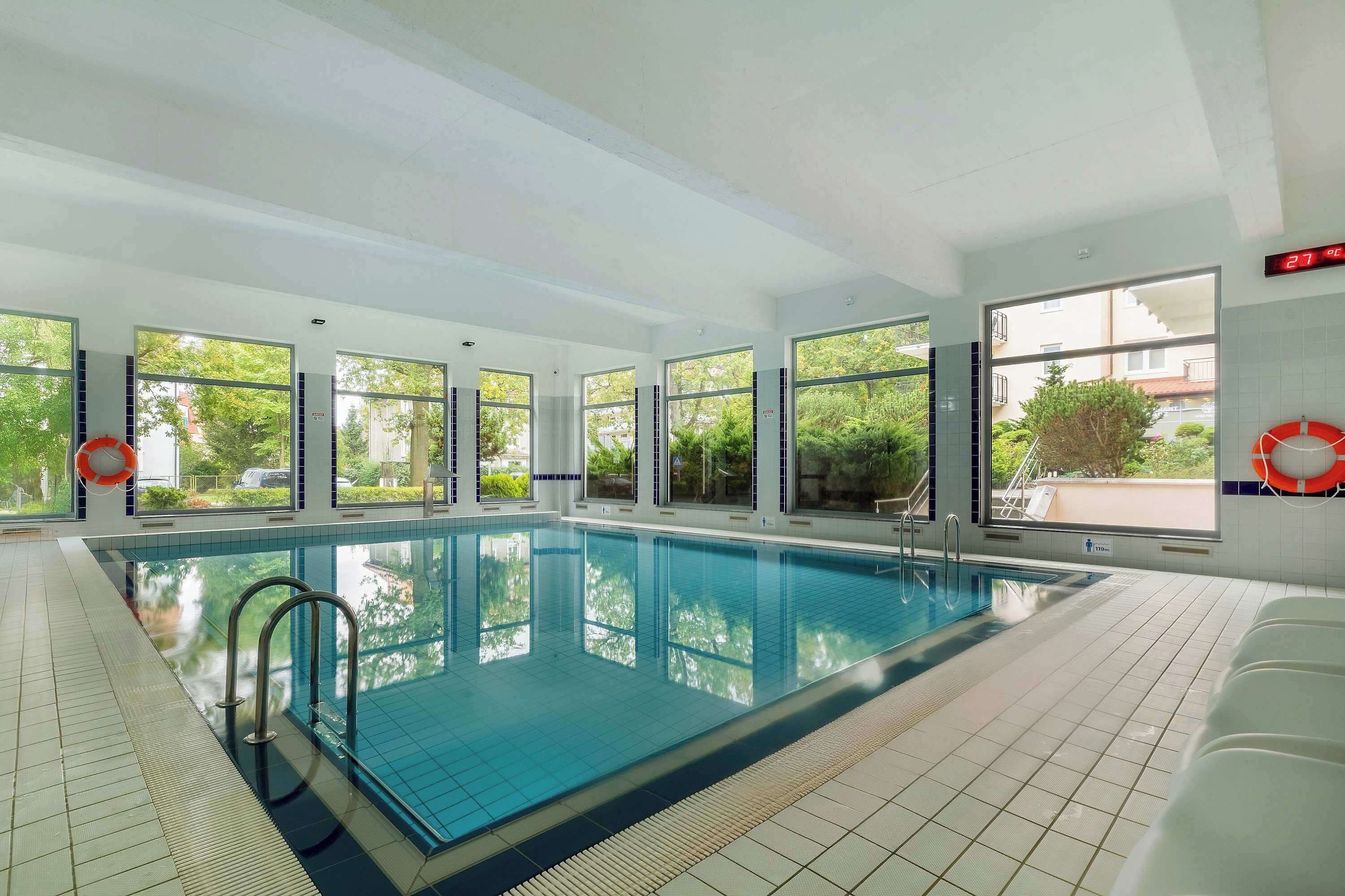 Ein Hallenbad mit großen Fenstern, Fliesenboden und einem Rettungsring an der Wand.