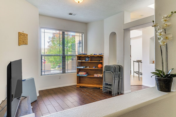 A living room with a flat-screen TV, a wooden bookshelf, and a potted orchid. - Room to Gather 13 Mi From Balloon Fiesta (Rio Rancho)