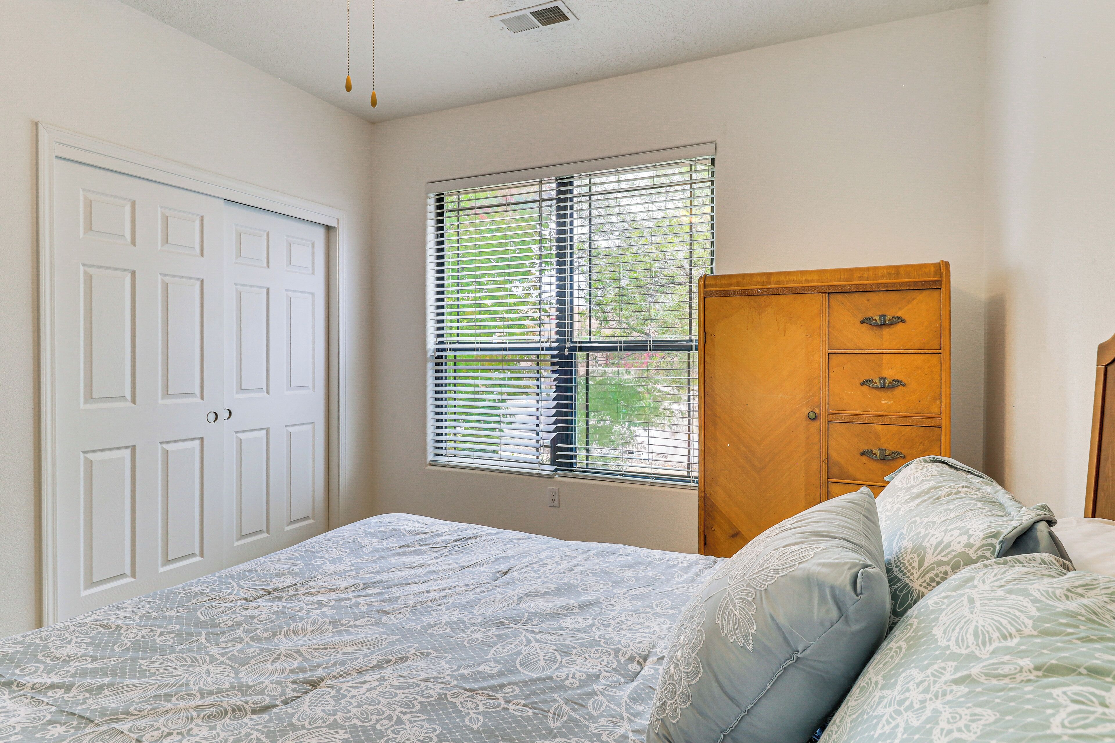 A bedroom with a bed, a wooden dresser, and a window with blinds.