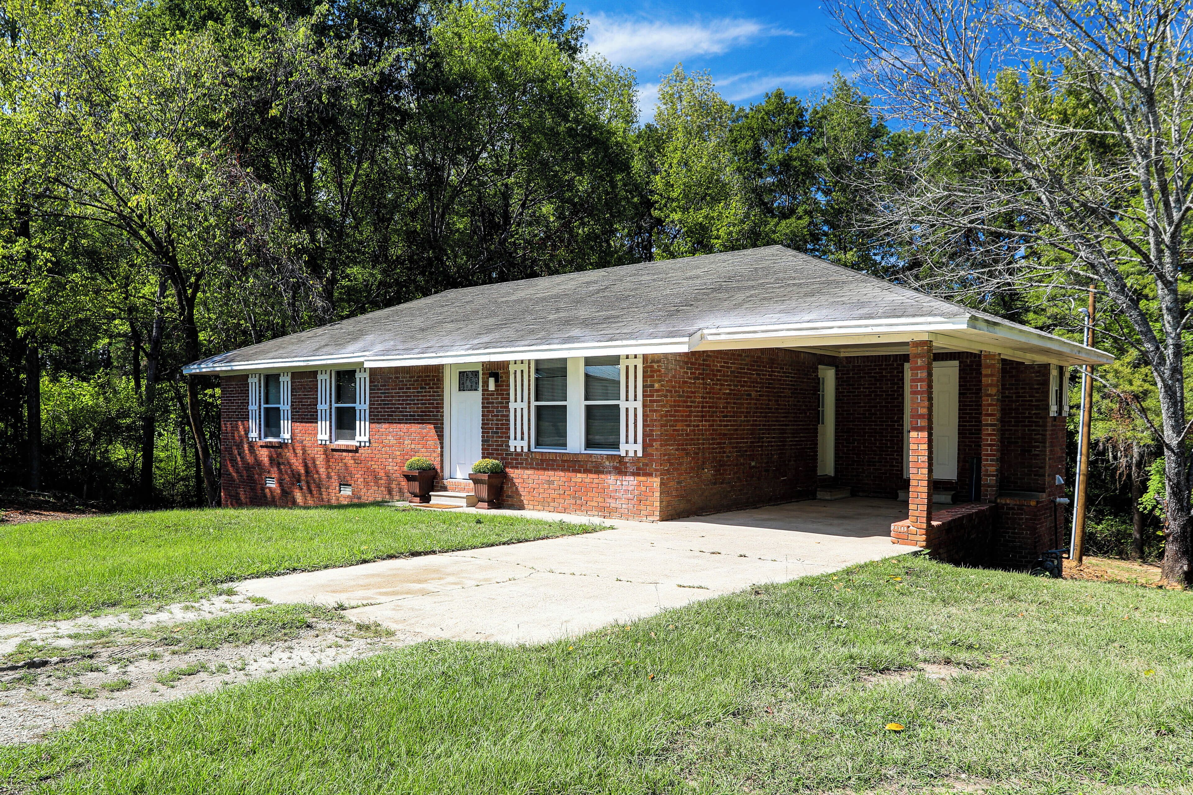 A single-story brick house with a front porch, a small front yard, and a clear sky.