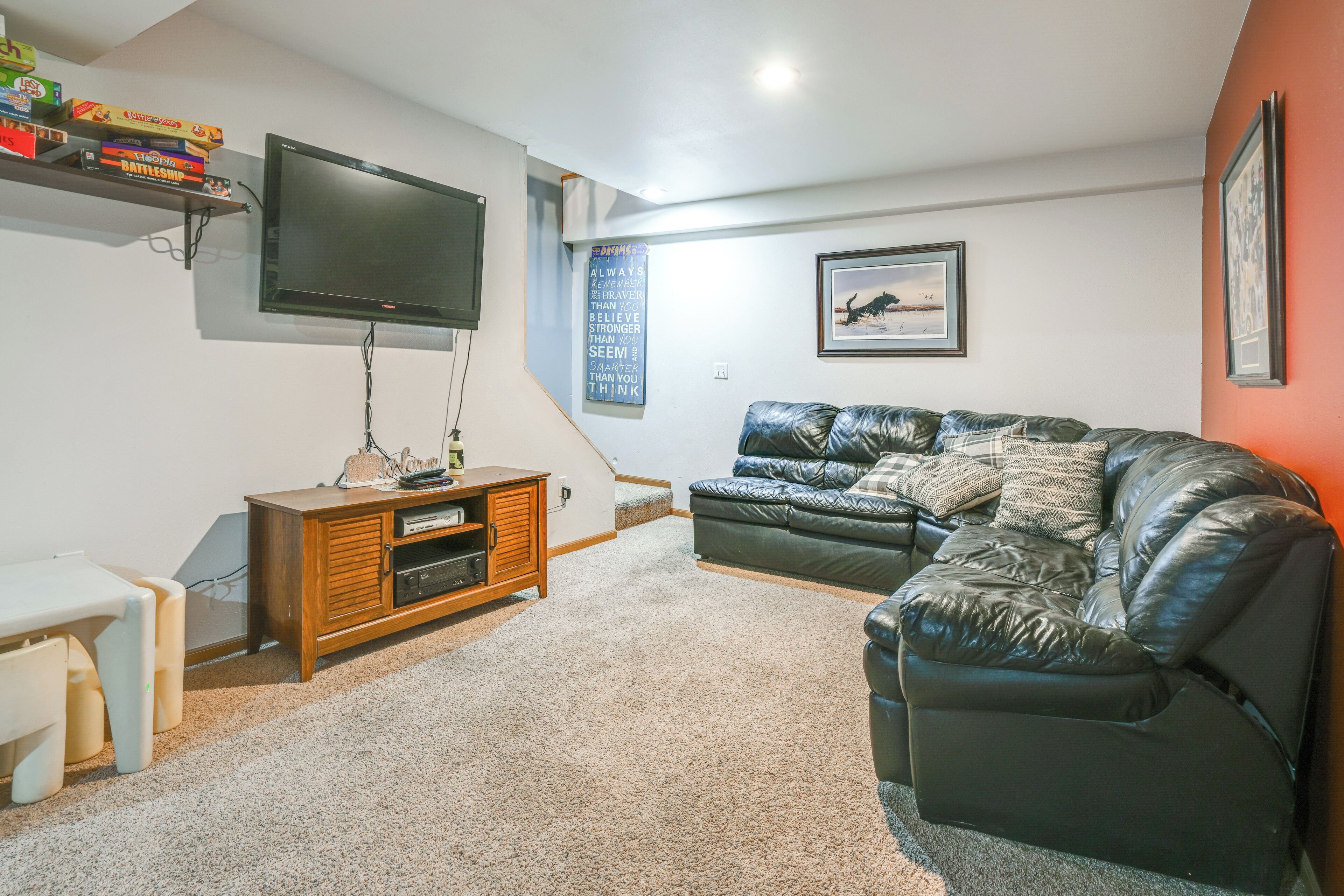 A living room with a flat-screen TV, a wooden entertainment unit, a leather sofa, and a framed picture on the wall.