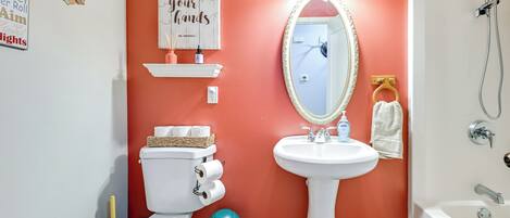 A bathroom with a toilet, sink, and shower. There are toilet paper rolls, a soap dispenser, and a towel rack.