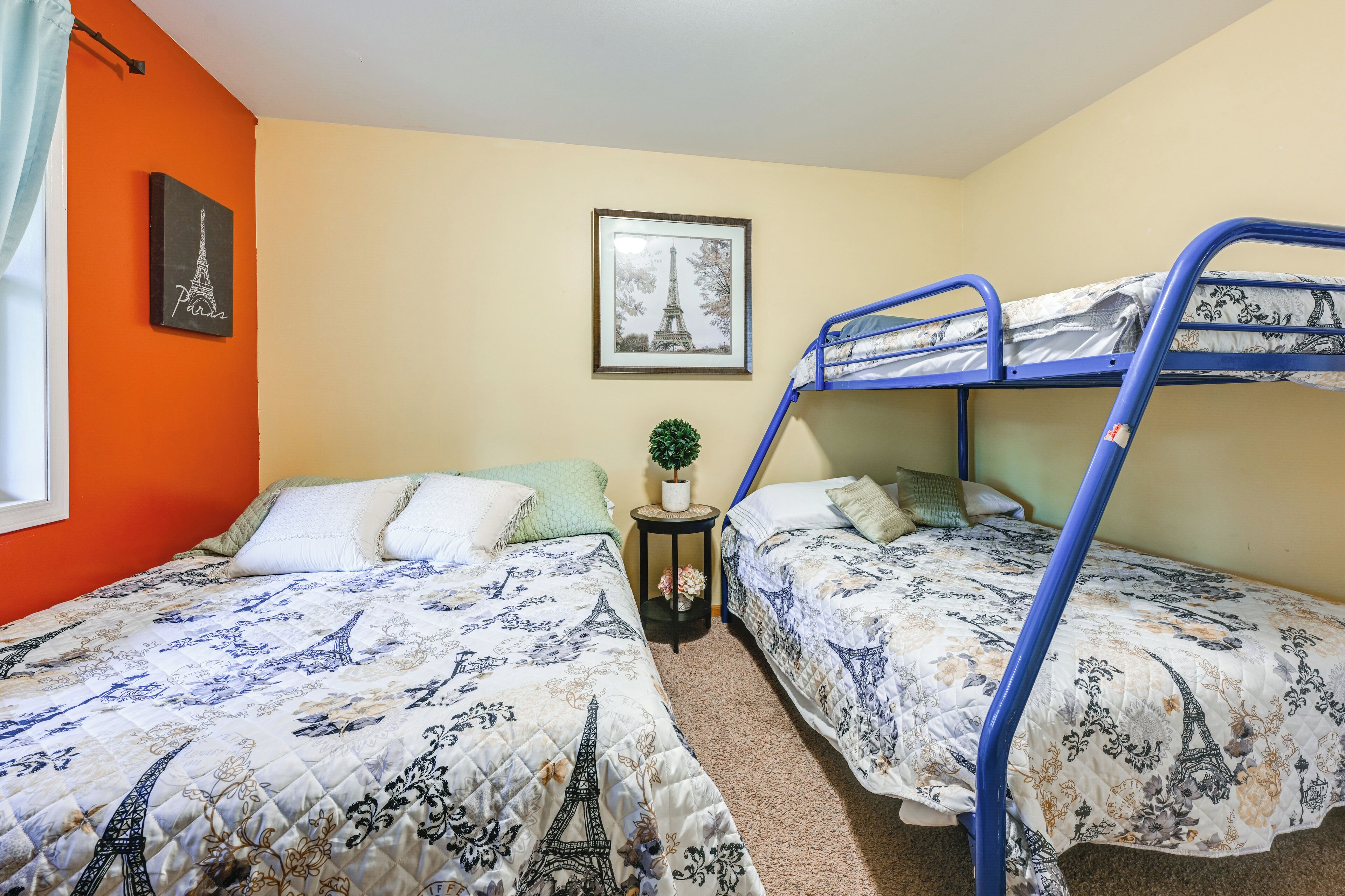 A room with two bunk beds, a small side table with a plant, and a framed picture of the Eiffel Tower on the wall.