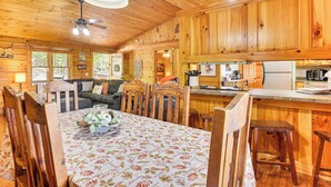 A wooden cabin interior with a dining table, chairs, a sofa, a kitchen area, and a ceiling fan. - Deck & Mtn Views: 'sunset Ridge Cabin' in Murphy (Murphy)