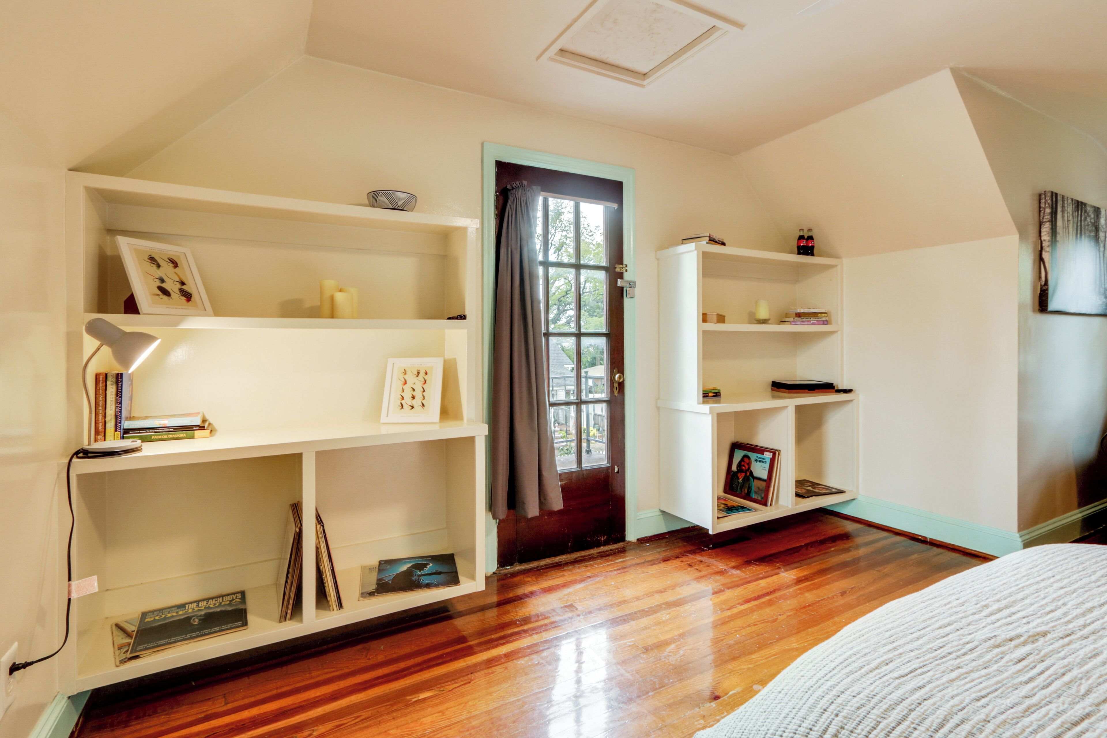 A room with wooden flooring, white shelving units, and a door with a curtain.