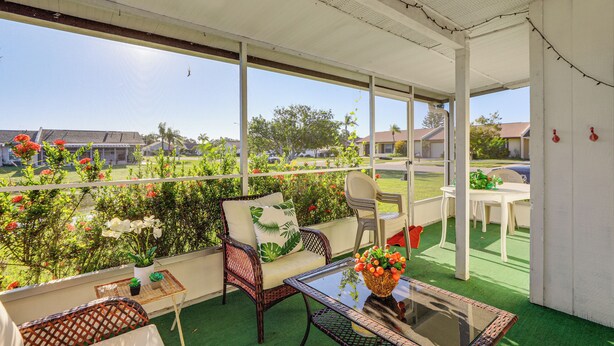 A covered patio area with wicker furniture, a glass table, and a view of a green lawn and buildings. - Pool Access: Condo 4 Mi to Bradenton Riverwalk! (Bradenton)