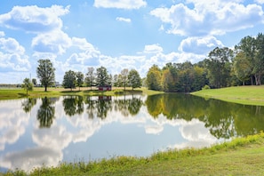 A serene landscape with a pond reflecting trees and a small building.