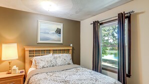 A bedroom with a bed, a nightstand, a lamp, a framed picture, and a window with curtains. - Fish, Unplug & Unwind! Countryside Plymouth Home (Plymouth)
