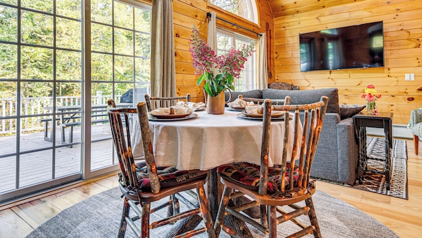 A wooden cabin interior with a dining table set for four, surrounded by wooden chairs.