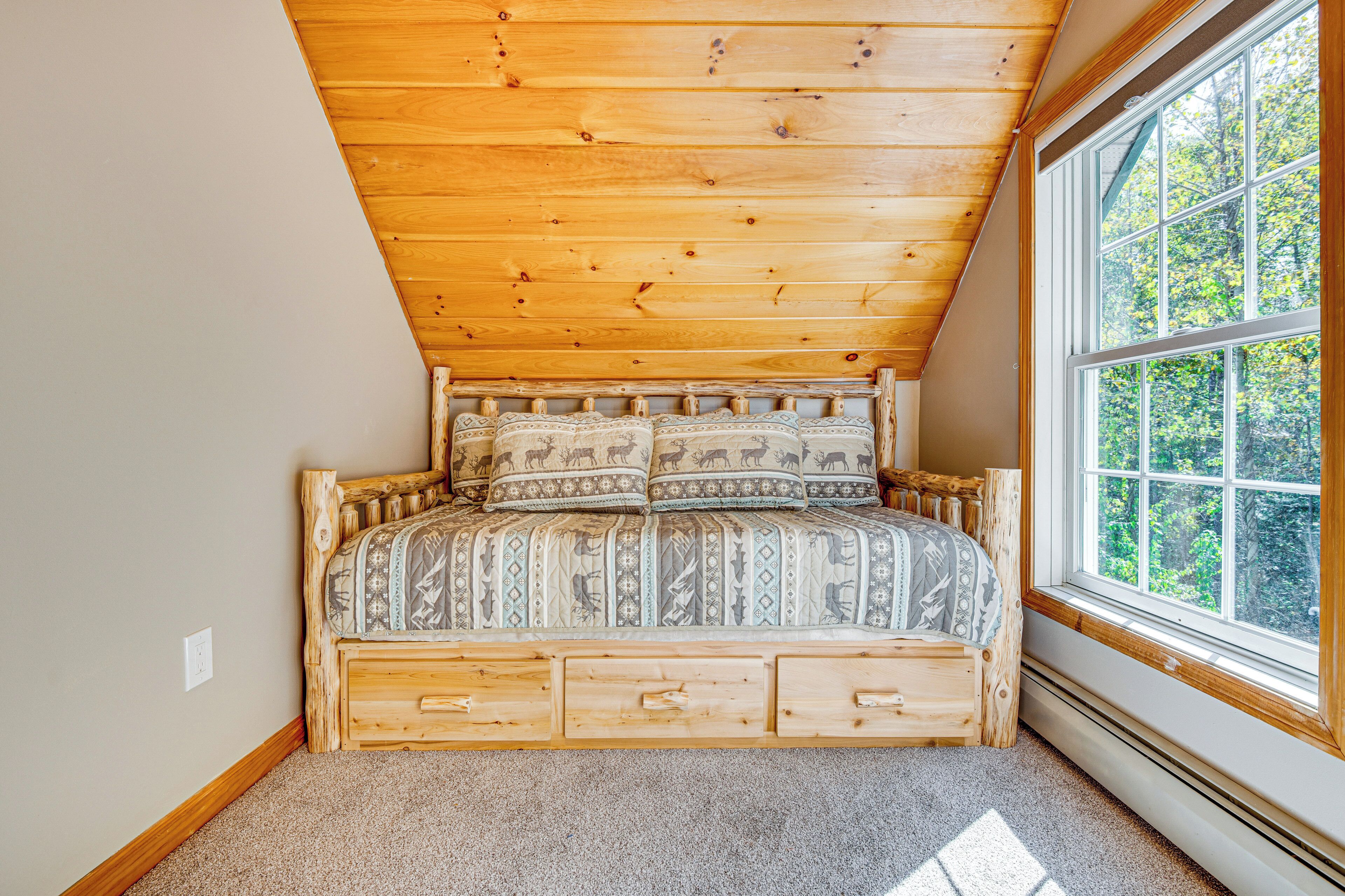 Une chambre avec un plafond en pente, une grande fenêtre et un lit en bois avec une literie à motifs.