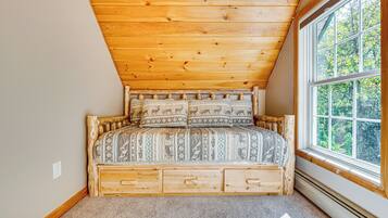 Une chambre avec un plafond en pente, une grande fenêtre et un lit en bois avec une literie à motifs.